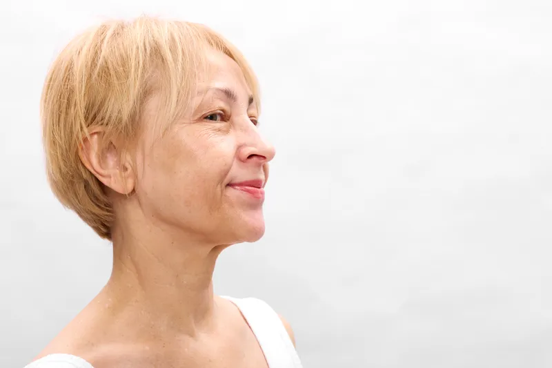 Senior woman profile smile portrait with short blonde hair, white background, calm relaxed expression, gentle studio lighting, wellbeing and beauty, serene self care