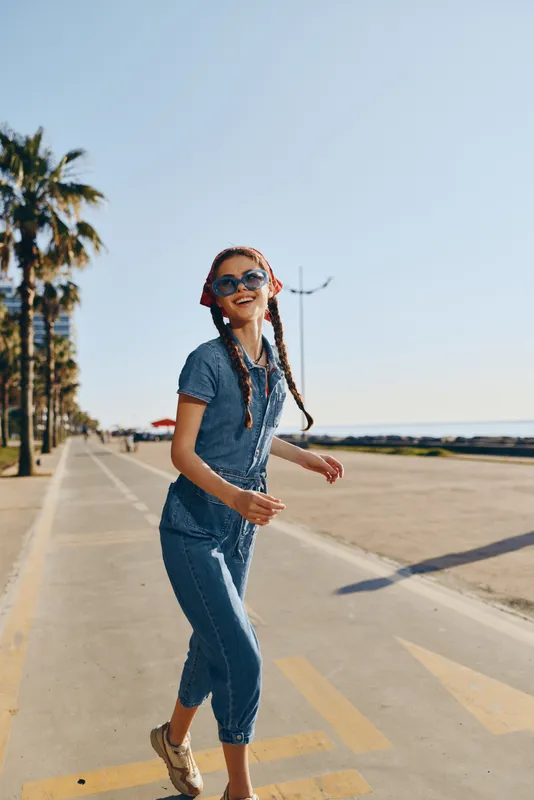 Lifestyle woman in modern boho-western denim street style smiling with sunglasses in warm natural sunlight, film color capturing vibrant urban fashion energy.