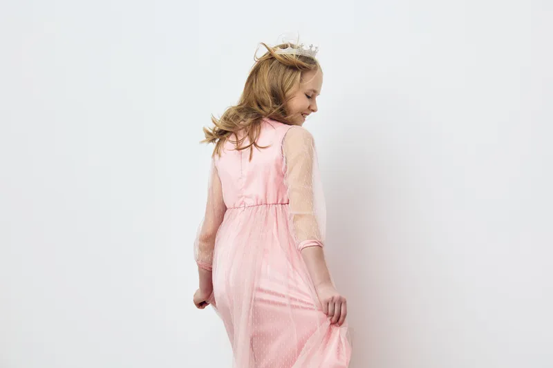 Charming young girl in a pink dress playful posing against a light background, showcasing innocence and joy, perfect for children s fashion and lifestyle concepts