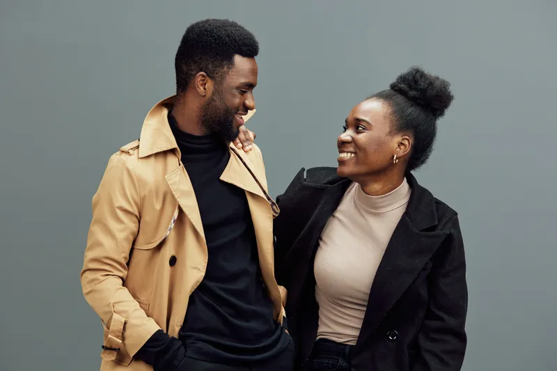 Happy couple smiling together, dressed in stylish outfits, against a neutral gray background, capturing love and connection in an urban aesthetic