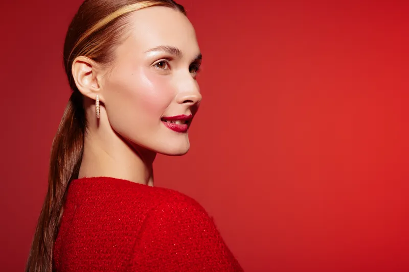 Young woman with long hair and red lipstick smiles confidently wearing red sweater against red background. Concept of beauty, fashion, elegance, and vibrant style portrait.