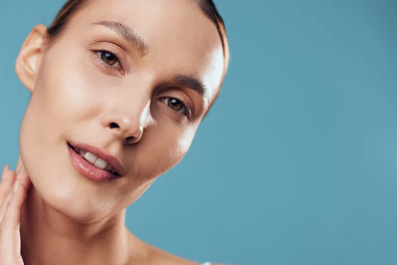 Young woman closeup portrait with natural makeup and glowing skin, relaxed in spa mood, skincare concept with hydration, soft light on face against blue background, clean care.