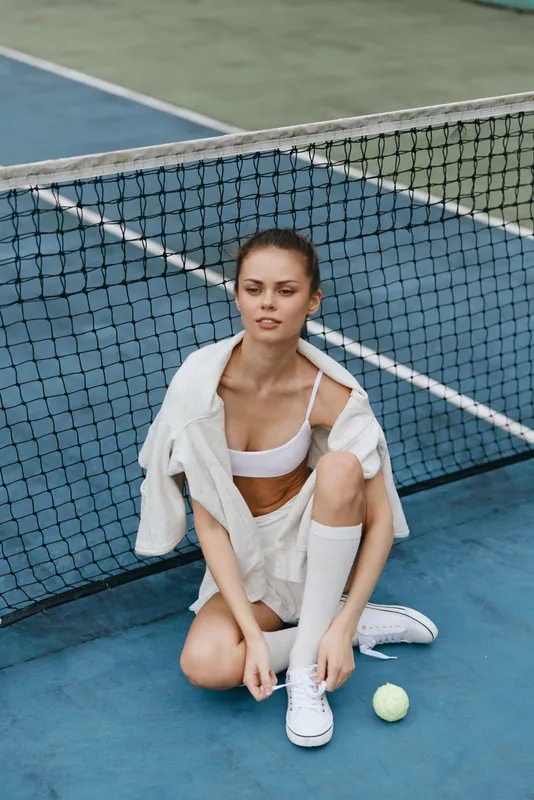 Young athletic woman in sports outfit sitting on tennis court, showcasing determination and readiness for action Tennis theme, green and blue colors dominate