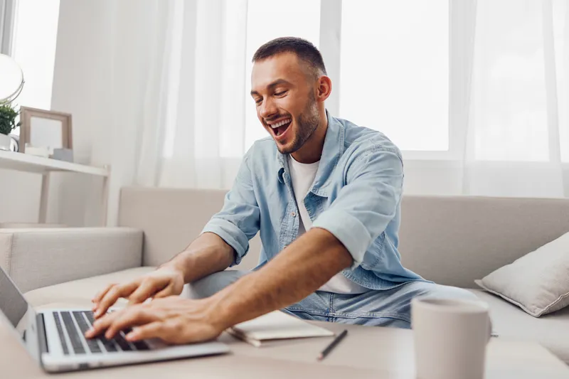 Happy man working on a laptop at home, enjoying a productive day. Modern interior with natural light creates an inspiring atmosphere for creativity.