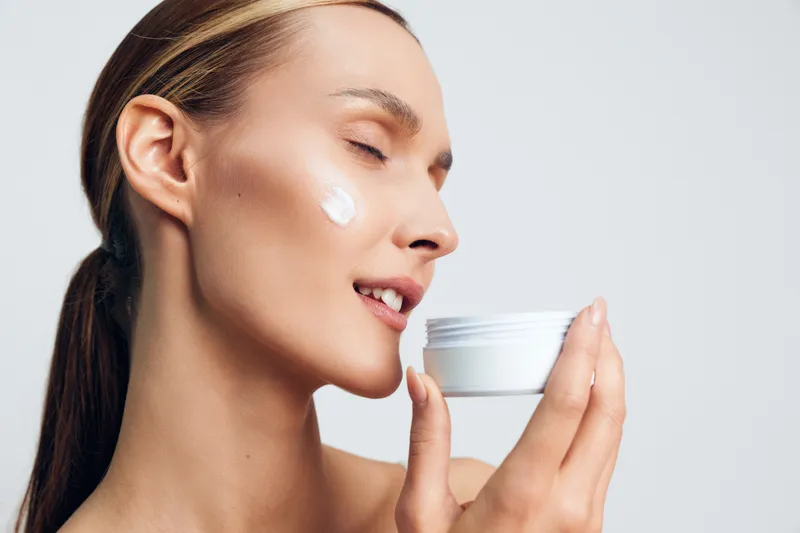 Woman applying face cream for skincare wellness, detail beauty care profile of a young female holding a white jar, soft studio light on clean white background, hydration and skincare routine