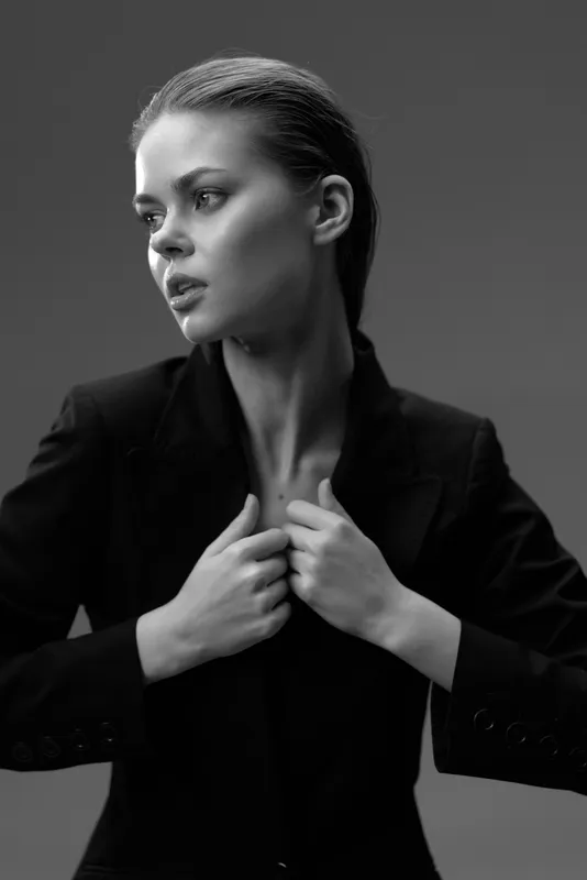 Black and white portrait of a thoughtful woman in a blazer with a serious expression and sleek hairstyle.