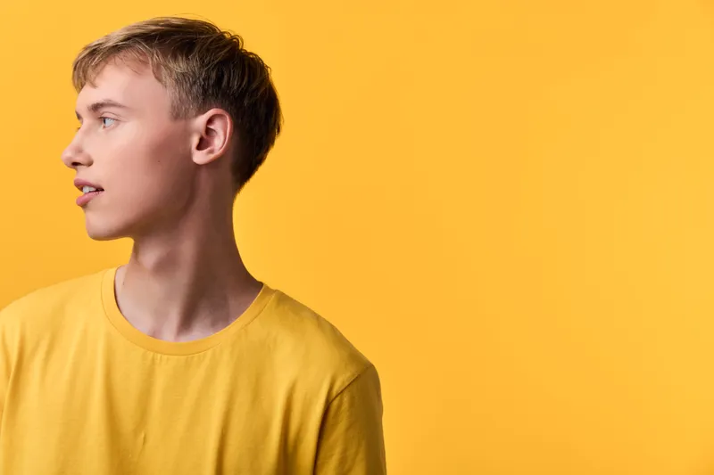 Young man yellow shirt gazing left against yellow background, a clean studio shot highlighting casual fashion, minimal design, color harmony, and a calm, focused mood