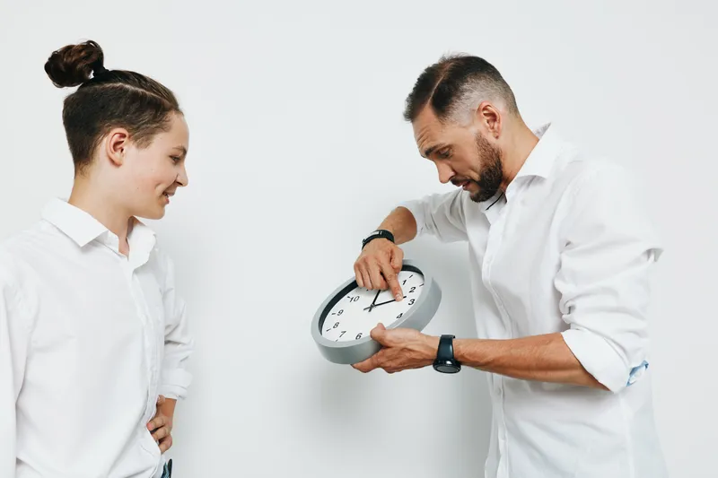 A professional business man demonstrates confident emotion while adjusting a wall clock against a clean, isolated colored background, conveying focus, timing, and precision.