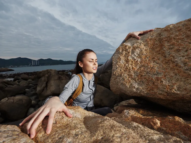 Young woman climbing rocks by the sea, showcasing determination and strength in an outdoor adventure setting Emphasizes resilience and exploration