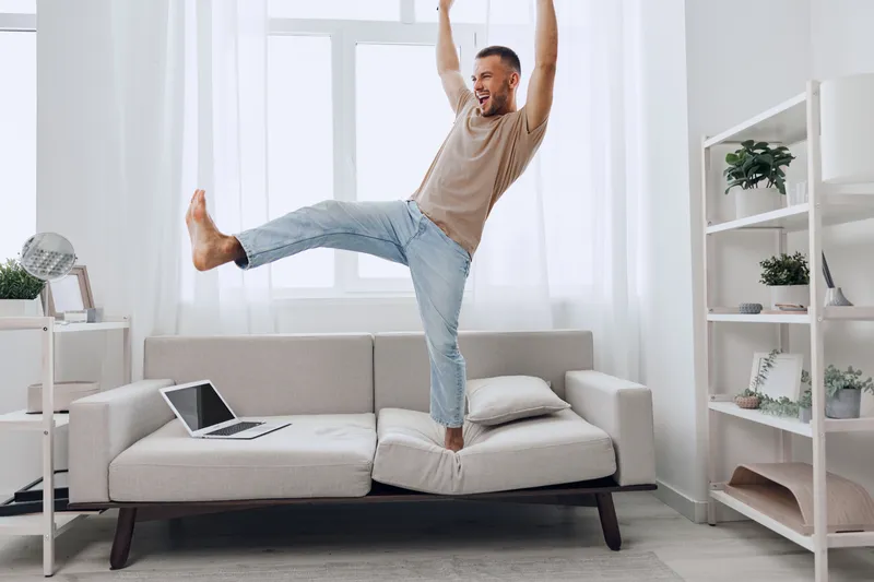 Joyful man enjoying a digital detox at home, blending work and relaxation while embracing moments of authentic imperfection in a light-filled space.
