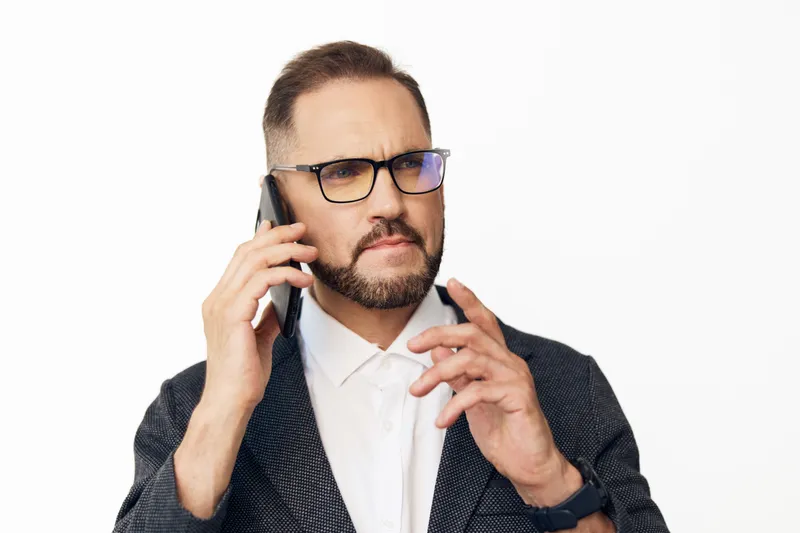 A focused business professional man talks on a mobile phone, showing determination and calm confidence. He stands against an isolated colored backdrop, conveying expertise, strategy, and strong