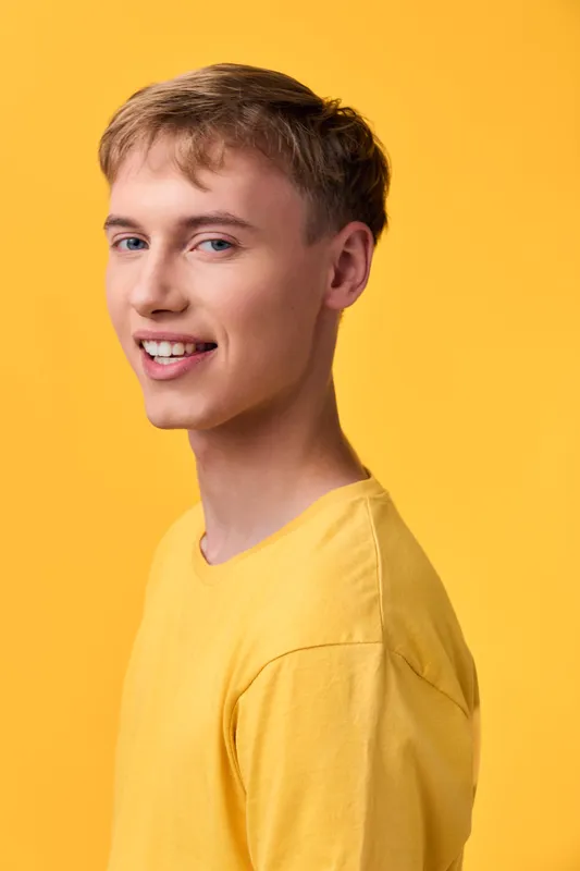 Young man in a yellow shirt with a bright yellow backdrop, smiling warmly, casual style and studio lighting for upbeat fashion imagery