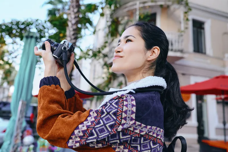 Camera in hand, outdoor street scene with a stylish woman captures candid, colorful moments and textured layers of architecture and cafe life in a lively urban backdrop