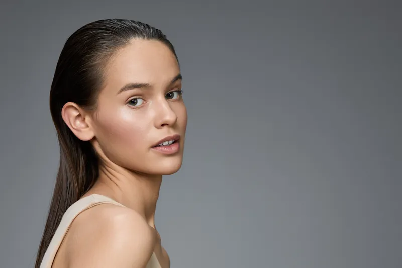 Young female model with long hair in neutral outfit, showcasing natural beauty and confidence against a soft gradient background
