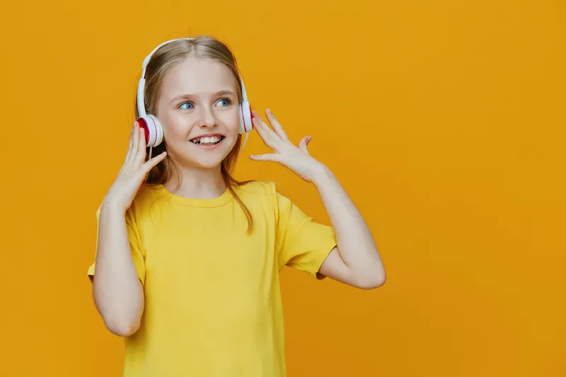 Happy young girl listening to music with headphones on a vibrant yellow background, showcasing joy, youthfulness, and a playful atmosphere