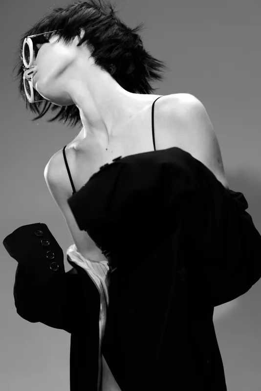 Black and white artistic portrait of a stylish woman wearing sunglasses and a black outfit with a dramatic pose and modern fashion vibes.