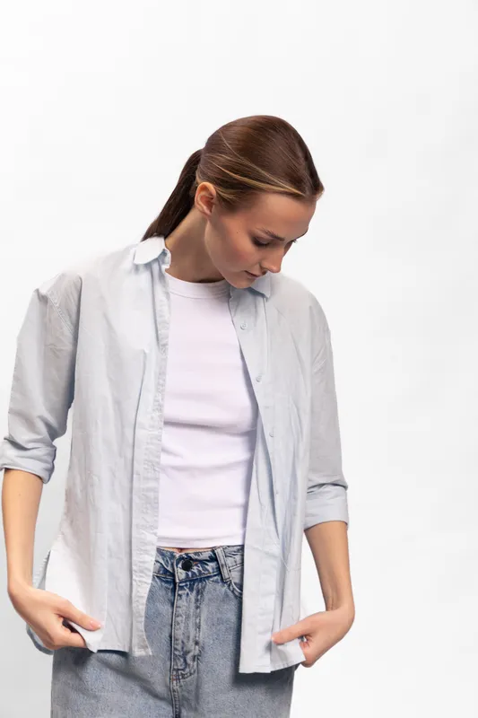 Young woman in casual outfit looks down with hands in pockets against white background. Concept of fashion, relaxation, and natural style with soft lighting and simple composition.