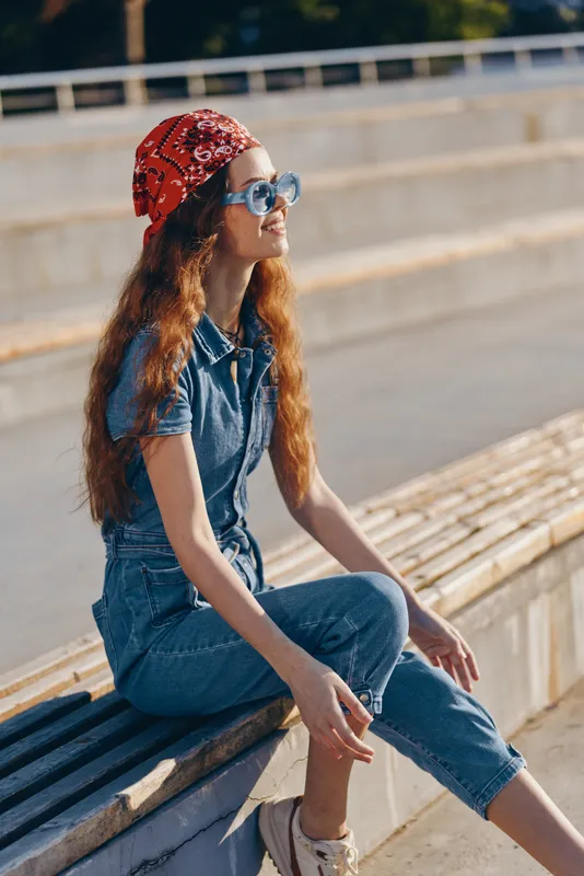 Lifestyle woman in modern boho-western denim street style wearing sunglasses and a red bandana, enjoying sunny urban outdoor atmosphere with film color effect.