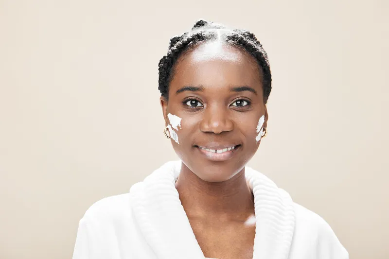 Smiling woman with natural skin care cream on her face, wearing a cozy white robe, showcasing healthy beauty and self care
