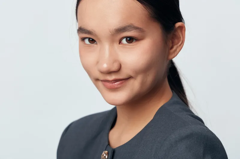 Young woman portrait with smile and natural makeup in business attire on light background. Asian female model with dark hair looking at camera for professional headshot or profile.