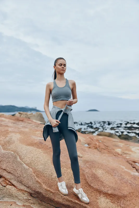 Confident young woman in sportswear showcasing an active lifestyle against a coastal backdrop, ideal for fitness and wellness themes