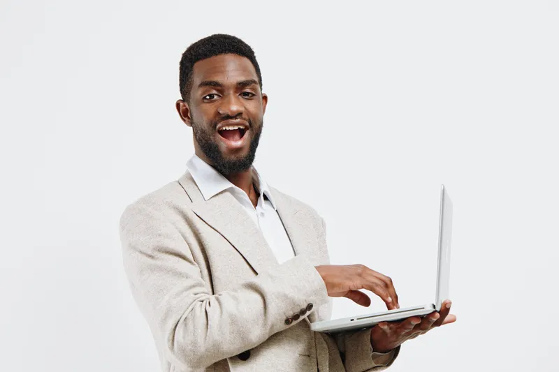 Smiling man holding a laptop computer in his hand, wearing a beige blazer and white shirt, looking cheerful, confident, and professional, isolated on a plain white background, studio portrait, busines
