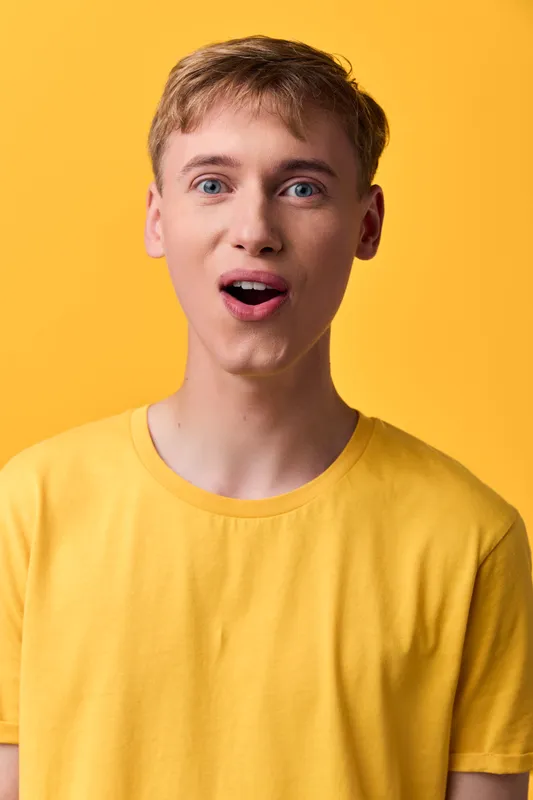 Surprised expression of a man in a yellow shirt, closeup in studio, bright lighting capturing excitement, astonishment and a dynamic reaction with clear facial features