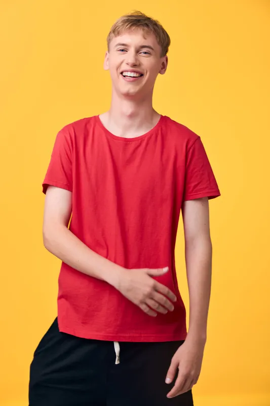 Smiling man in a red t shirt stands against a bright yellow background, radiating casual confidence and friendly energy for lifestyle, fashion or advertising imagery