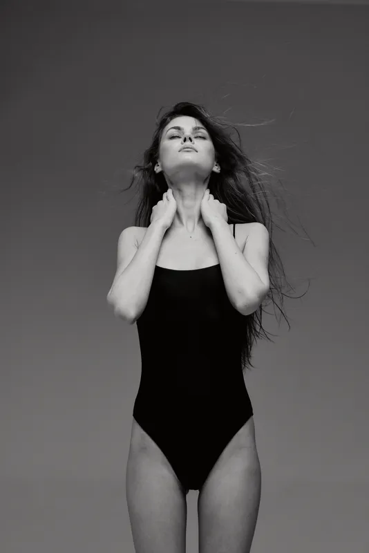 Black and white portrait of a woman in a swimsuit with closed eyes and flowing hair against a plain sky background