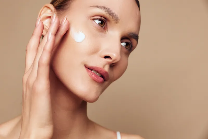 Closeup of woman applying face cream, smooth skin texture, natural makeup, soft lighting, neutral background, skincare routine, gentle touch, healthy complexion