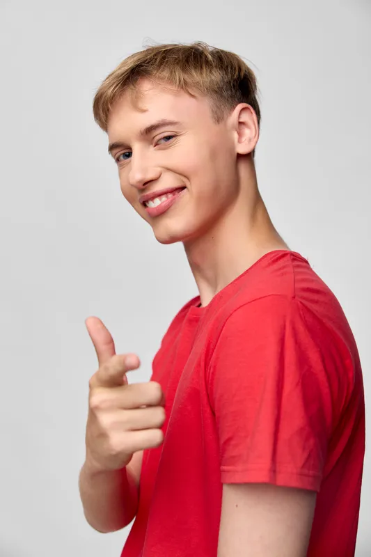Smiling young man in a red t shirt points playfully at the camera, casual studio vibe, confident and approachable, ideal for lifestyle marketing, social media, and cheerful engagement