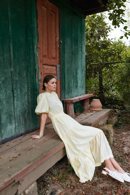 Woman in flowing dress on rustic porch bench, countryside relaxation scene with authenticity and inclusivity