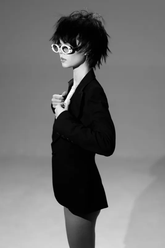 Black and white portrait of a stylish woman with short hair wearing sunglasses and a blazer, displaying confident and modern attitude.
