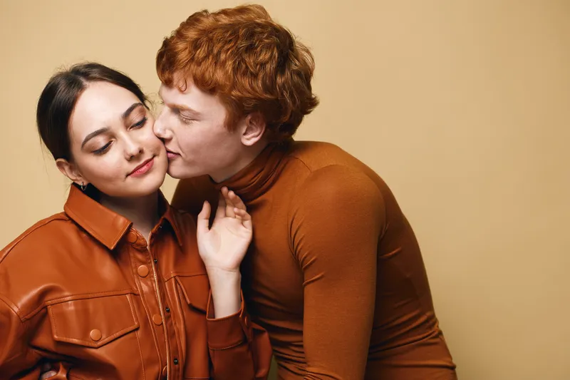 Couple, intimacy, love and affection with young man and woman expressing tenderness and connection in casual stylish clothes against beige background in studio.