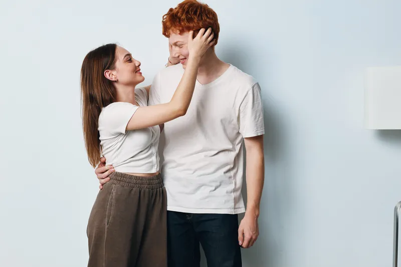 Couple, love, happiness and intimacy with woman touching man face, smiling and hugging at home with casual clothes in bright room and cozy atmosphere together.