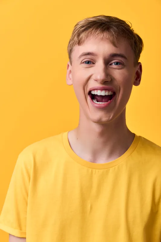 Smiling, young, man in yellow shirt conveys happiness and energy bright background casual style highlighting positive friendliness vibrant mood and approachable vibe for lifestyle marketing and