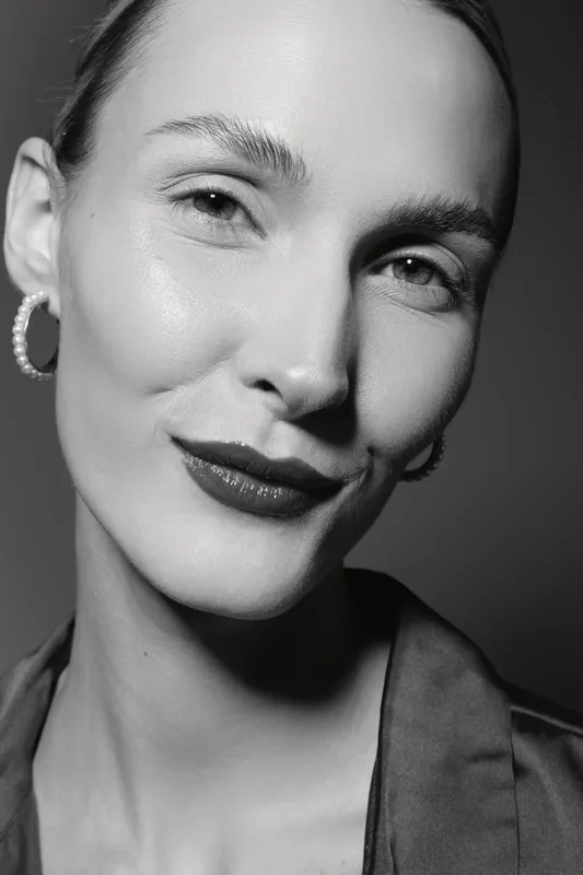 Close-up portrait of a smiling white woman with fair skin and pearl earrings in monochrome. Concept for beauty, confidence, and skincare in studio lighting.