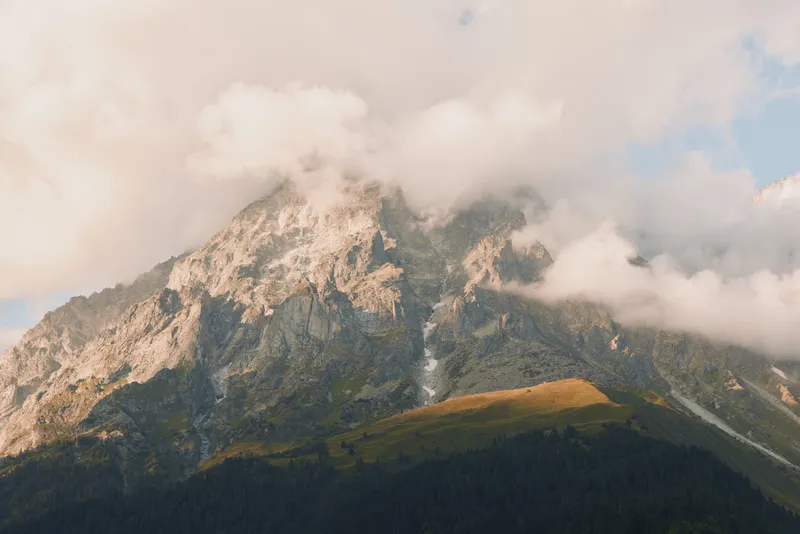 Majestic mountain landscape with clouds over rugged peaks, alpine slopes and pine forests, a tranquil outdoor nature scene perfect for travel and adventure shooting