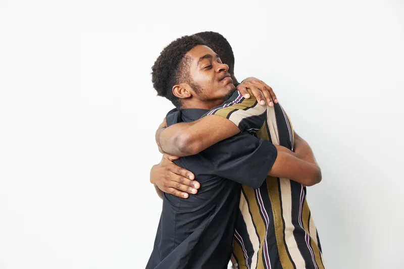Two African American men embracing each other, showcasing strong friendship and love. Their warm expressions capture a sense of unity and connection.