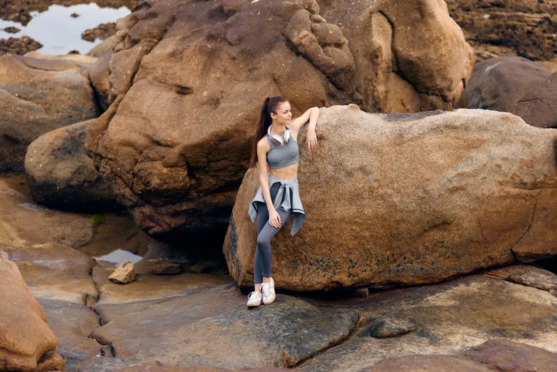 Athletic woman in activewear posing on rocky beach, conveying confidence and strength, perfect for fitness and healthy lifestyle concepts