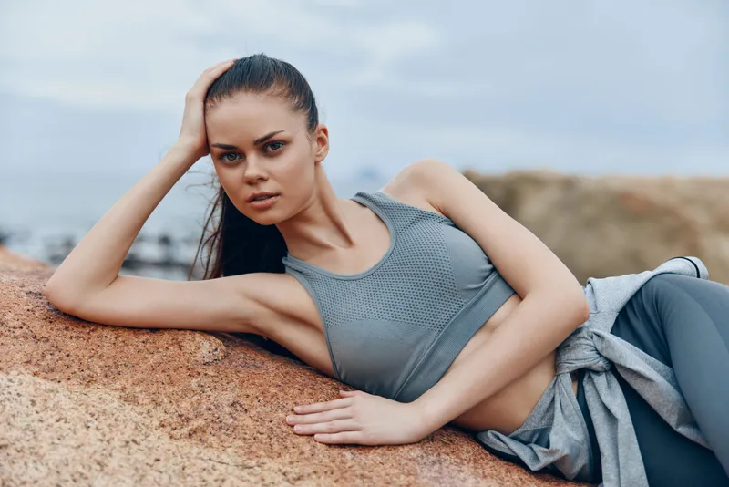 Athletic woman in gray sportswear posing outdoors, showcasing confidence and strength against a natural rocky background Fitness, determination, nature, health, sports