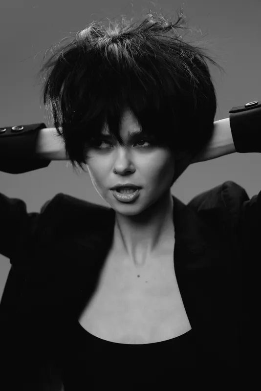 Black and white portrait of a young woman with short hair posing confidently in dark clothing