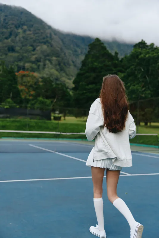 Young female athlete walking on a tennis court in a serene outdoor setting, showcasing athletic wear, emotions of focus and determination, with a soft color palette