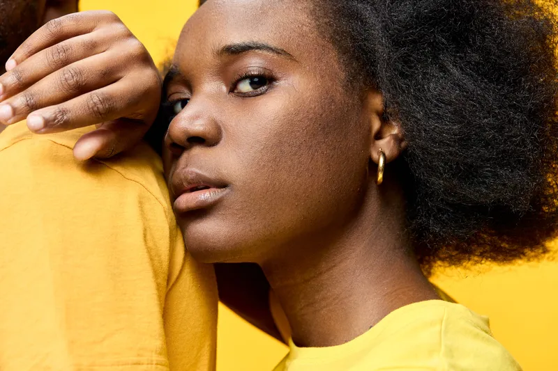Close up portrait of a young Black woman with natural hair embracing a partner, wearing yellow clothing against a bright yellow background, conveying warmth and connection