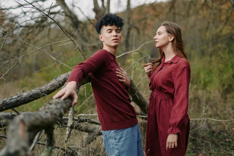 Two friends stand in a natural setting, wearing burgundy outfits, conveying authenticity through candid pose and genuine connection in soft outdoor light.