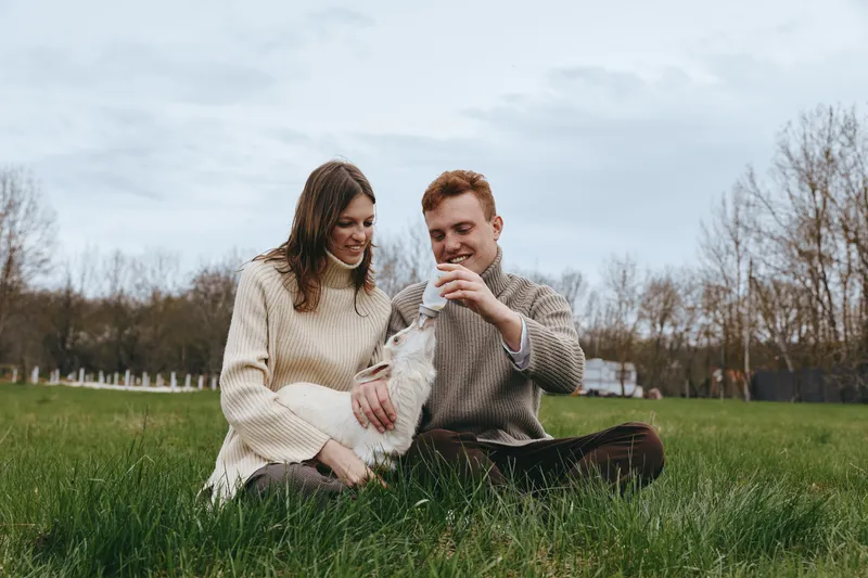 couple outdoors lifestyle dog meadow grass sweater happiness relaxed candid nature joyful affection companionship sunlight greenery field scenery moment bonding warmth park breeze comfort casual