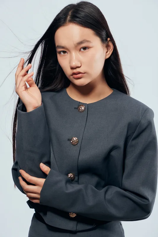 Young woman with long black hair and serious expression wearing a dark gray jacket with buttons studio portrait on light background. Fashion, beauty, model and style concept.