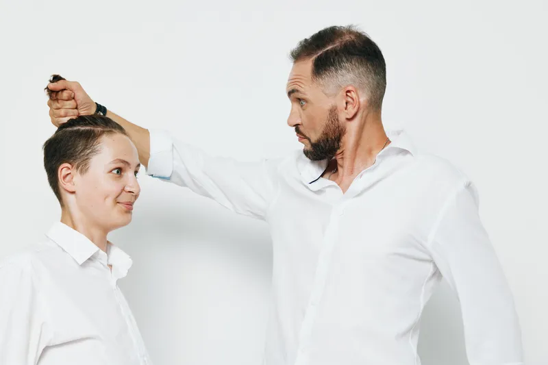 A focused male business professional demonstrates confident emotion as a colleague adjusts his tie against an isolated colored background, conveying leadership, teamwork, and professional poise.