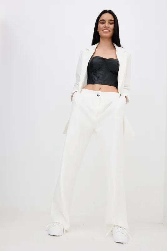 stylish woman wearing white pants and blazer with black top, posing confidently against plain white background, modern fashion and casual elegance.