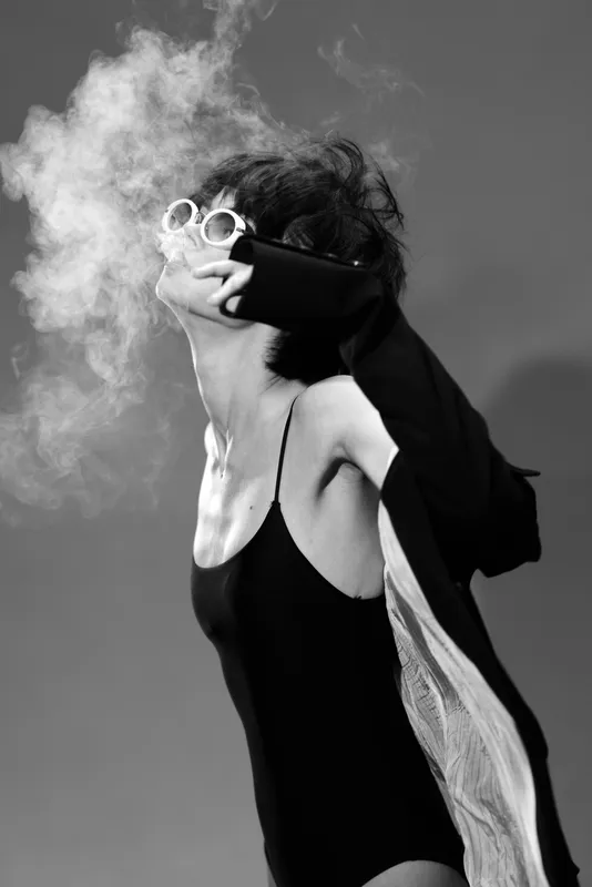 Black and white woman wearing sunglasses blowing smoke with stylish outfit and dynamic pose